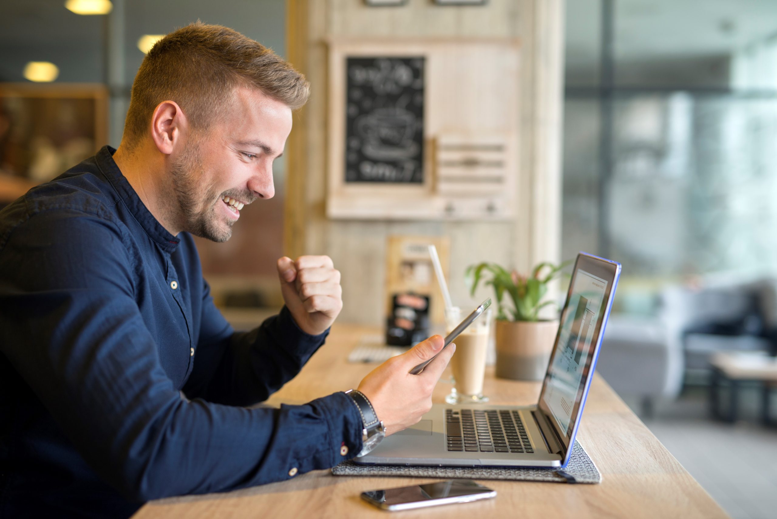 Happy freelancer with tablet and laptop computer in coffee shop.